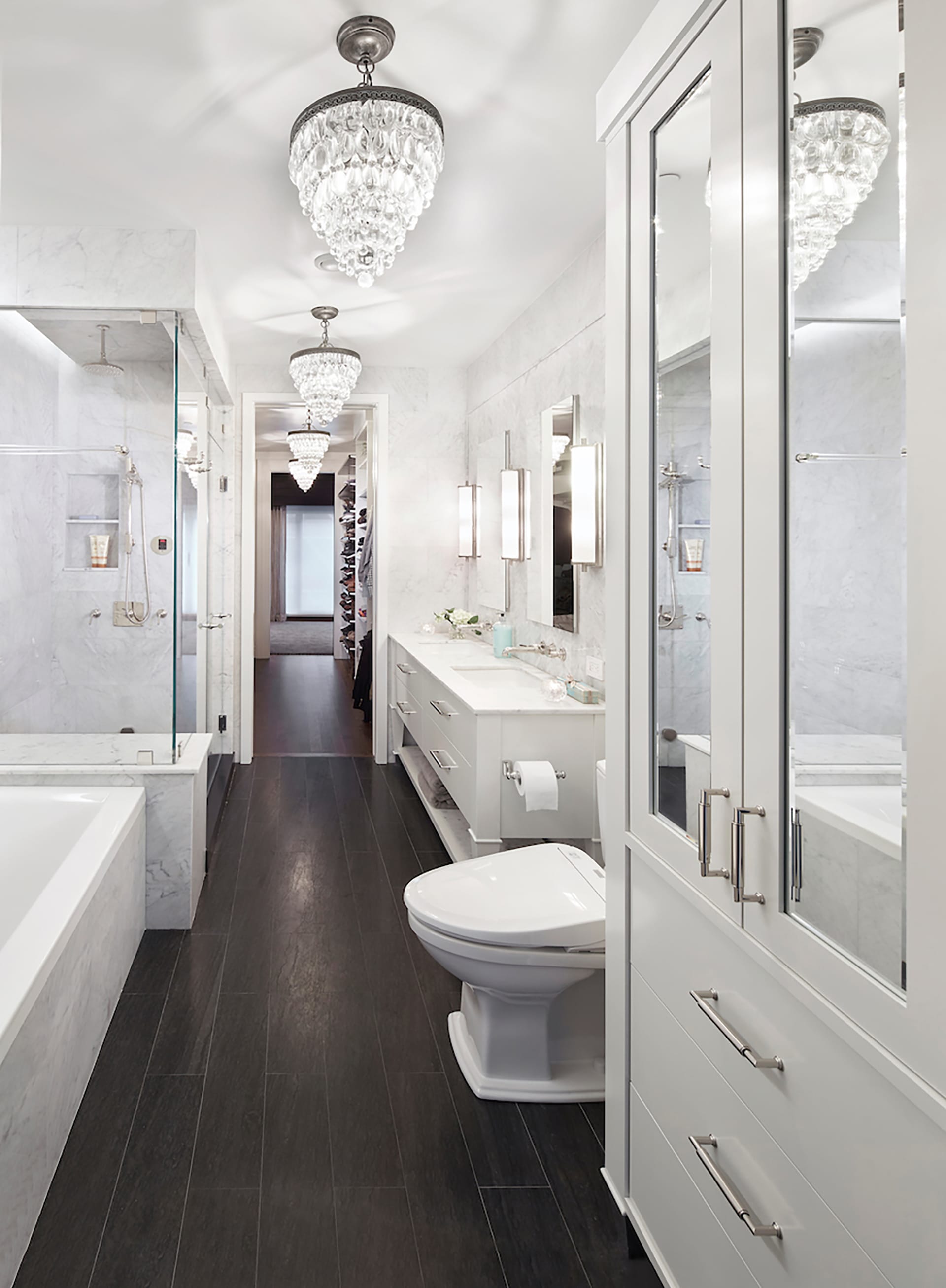 Primary bathroom with multiple chandeliers and marble floors and walls